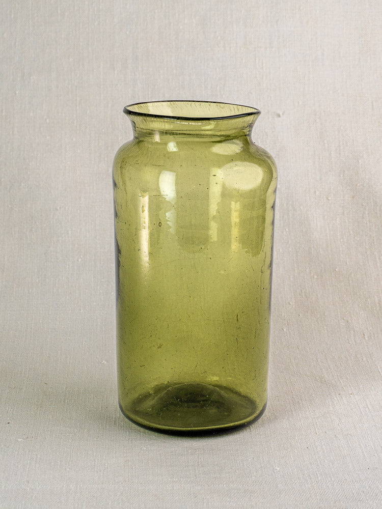 Antique French olive green glass preserve jar, late 18th century, tall cylindrical shape, flared rim, on textured surface.