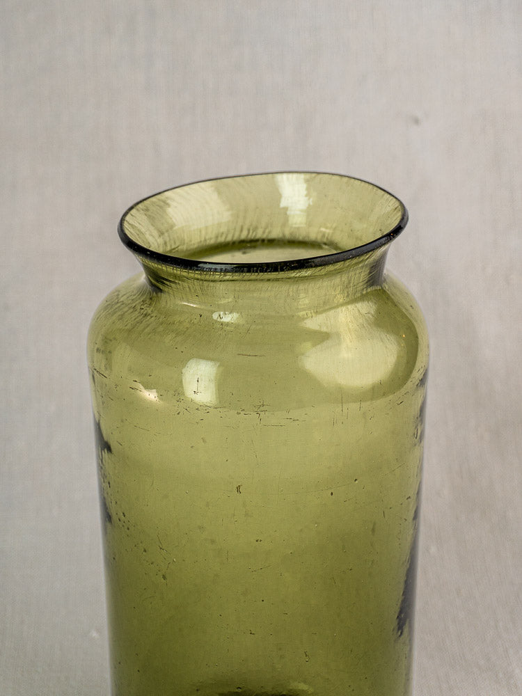 Antique French olive green glass preserve jar, hand-blown with wide flared rim, on a neutral light gray background.