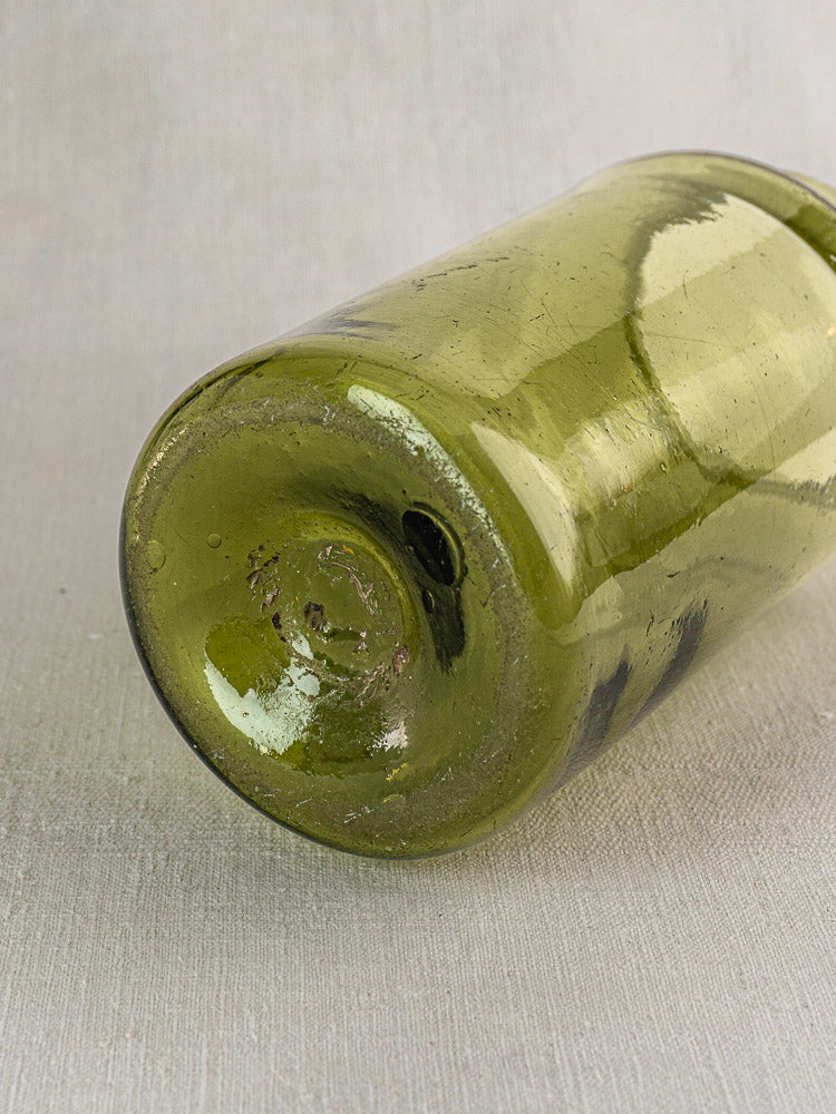 Antique French olive green hand-blown glass preserve jar base with bubbles on light gray textured surface.