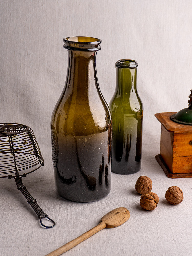 Antique French truffle jar, circa 1800, hand-blown olive glass with dark brown tone, on gray surface.