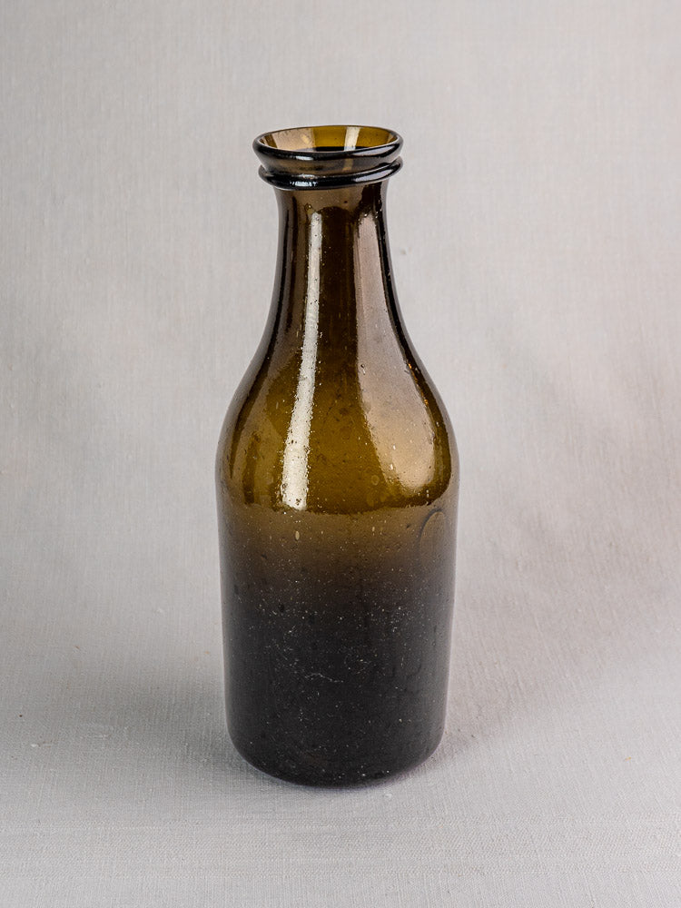 Antique French truffle jar, circa 1800, hand-blown olive glass with dark brown tone, on gray surface.