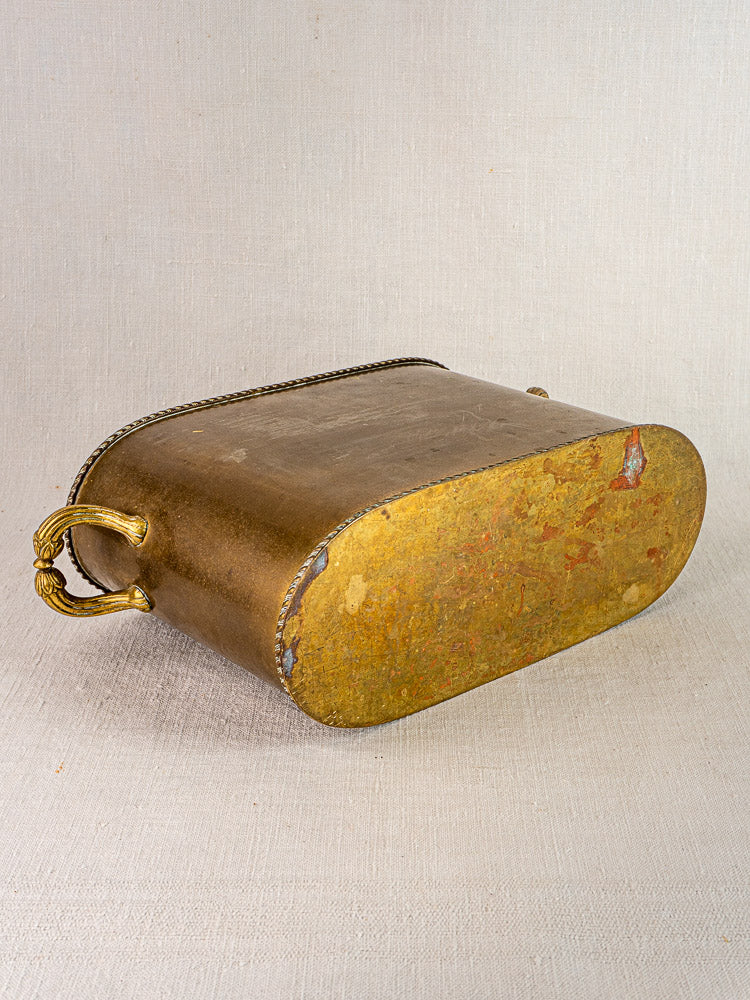 Antique French brass double champagne cooler with ornate rope handle, oval base exposed on neutral fabric.