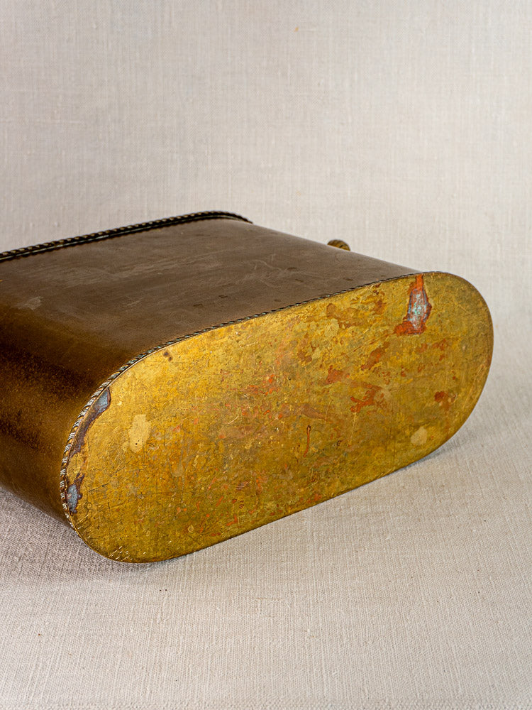 Close-up of antique French brass double champagne cooler base showing oval shape, tarnish, and wear on fabric.