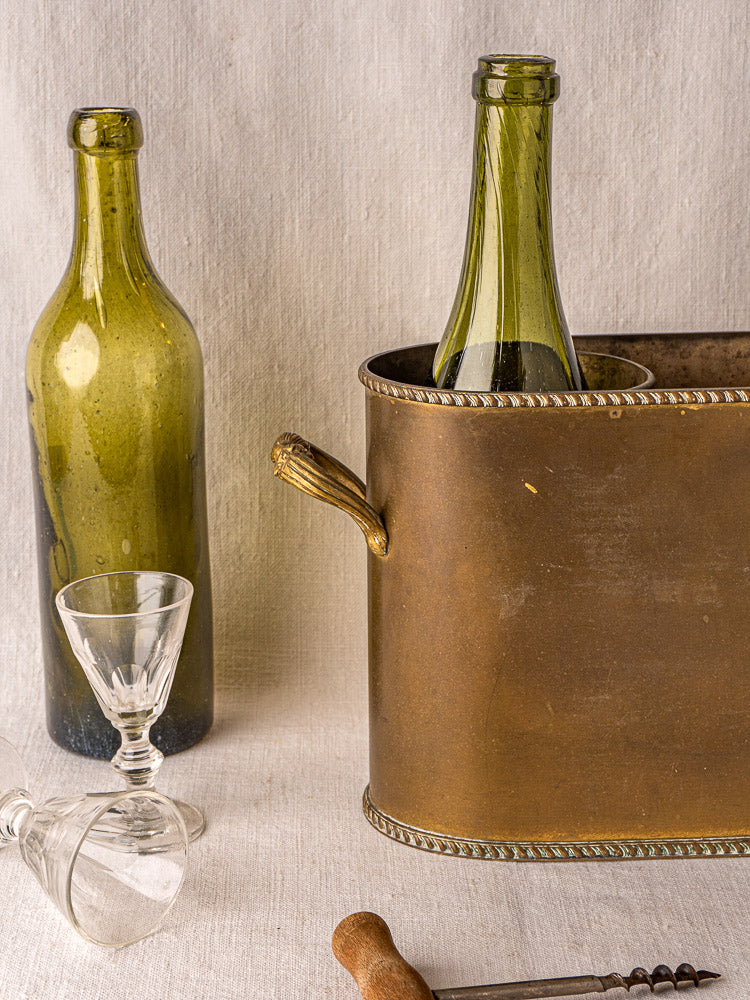Antique French brass double champagne cooler with two green wine bottles, glasses, and corkscrew.
