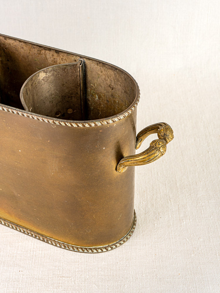 Antique French brass double champagne seau with lion head handles and rope-like trim on light fabric.