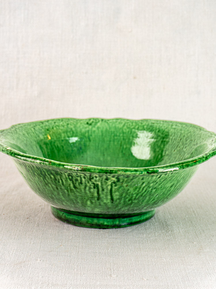 Vallauris ceramic bowl by Foucard-Jourdan with green glaze and wavy rim, shown on light fabric.