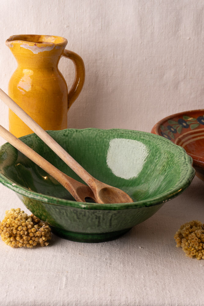 Green-glazed Vallauris bowl by Foucard-Jourdan in early 20th-century French style with wooden spoons and yellow dried flowers.