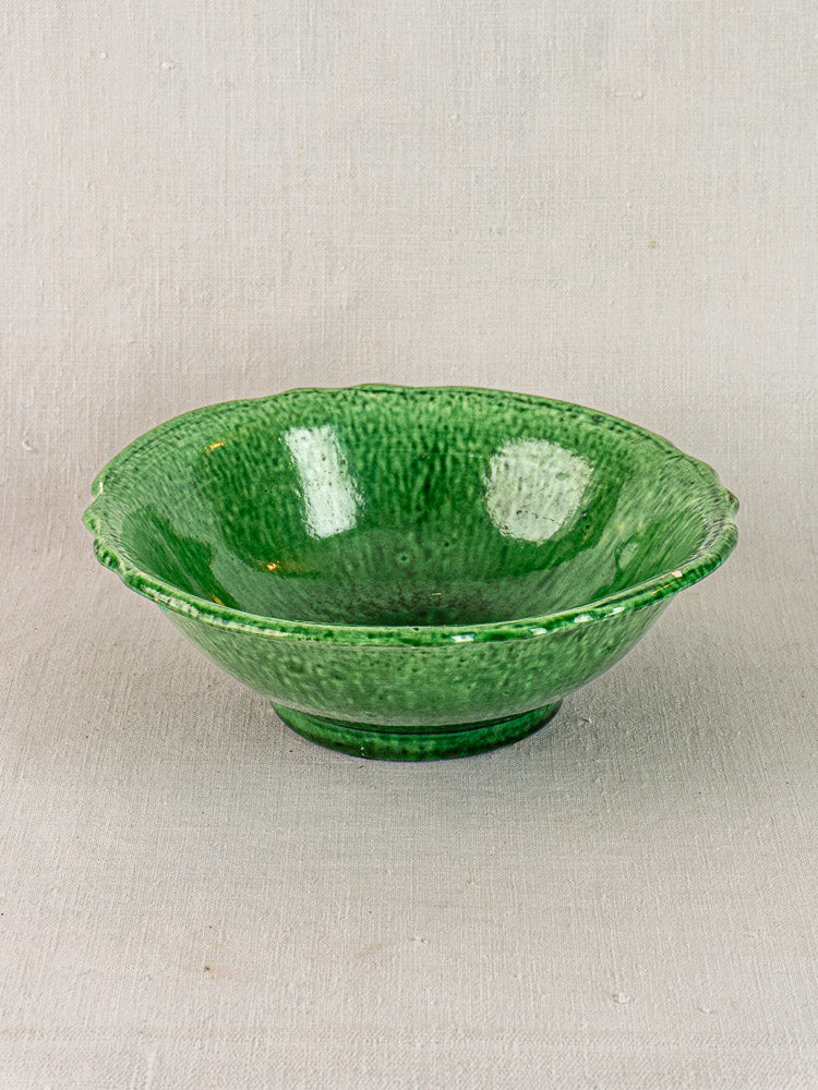 French Vallauris ceramic bowl by Foucard-Jourdan with green glaze and scalloped rim on beige fabric, early 20th century.