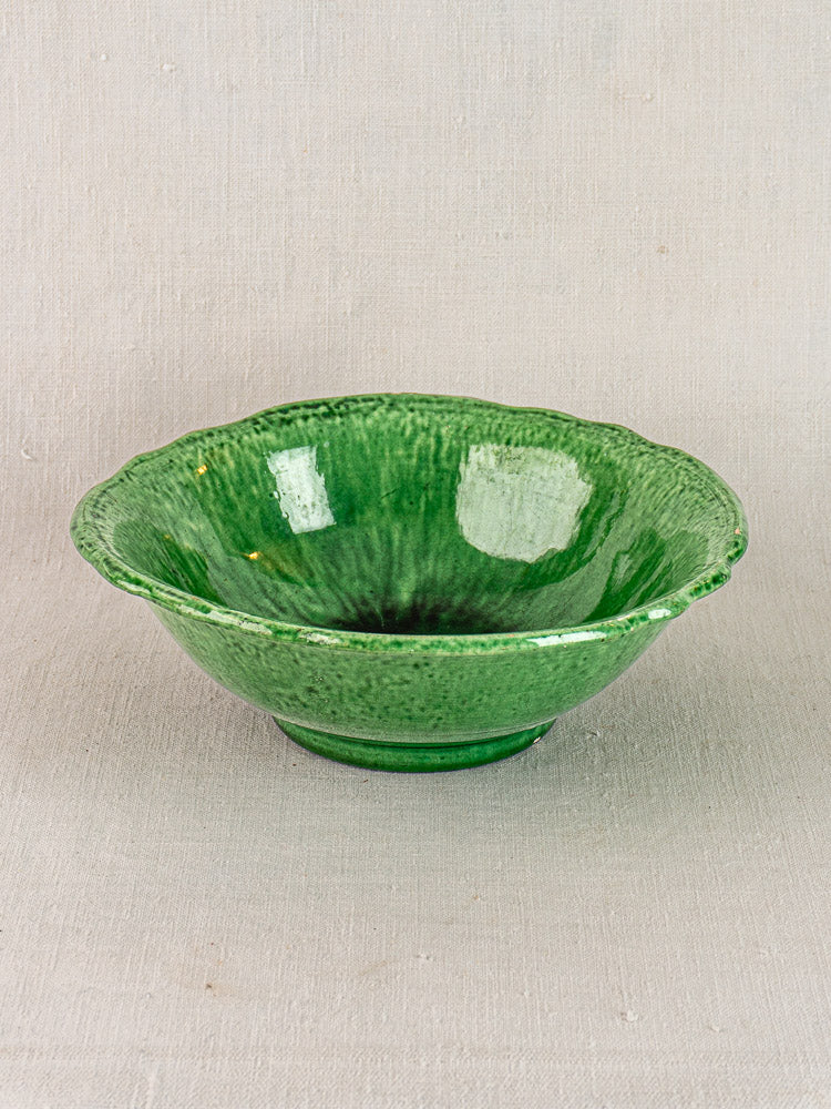 French Vallauris bowl by Foucard-Jourdan with green glaze and scalloped rim, early 20th century, on light fabric.
