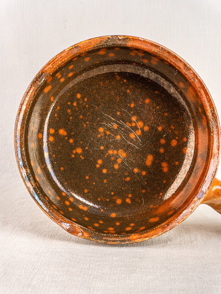 Antique French Vallauris Jaspé terracotta pan with brown glaze and orange speckles on fabric background.