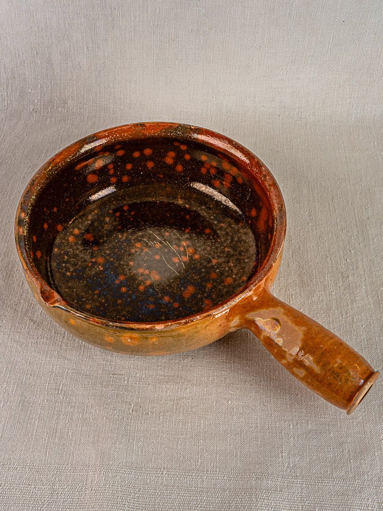 Antique Vallauris Jaspé Poêlon French terracotta cooking pan with brown ceramic and speckled interior on light surface.