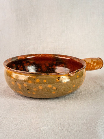 Antique French Vallauris Jaspé Poêlon terracotta pan with brown glaze, handle, and spout on fabric.