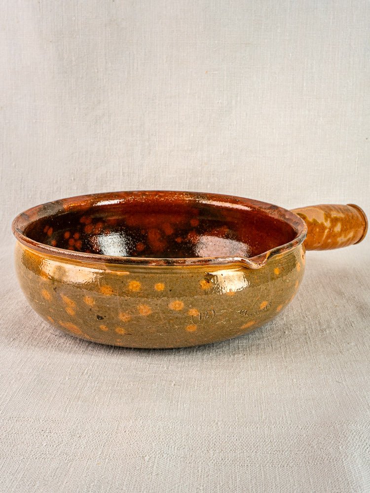 Antique French Vallauris Jaspé Poêlon terracotta pan with brown glaze, handle, and spout on fabric.
