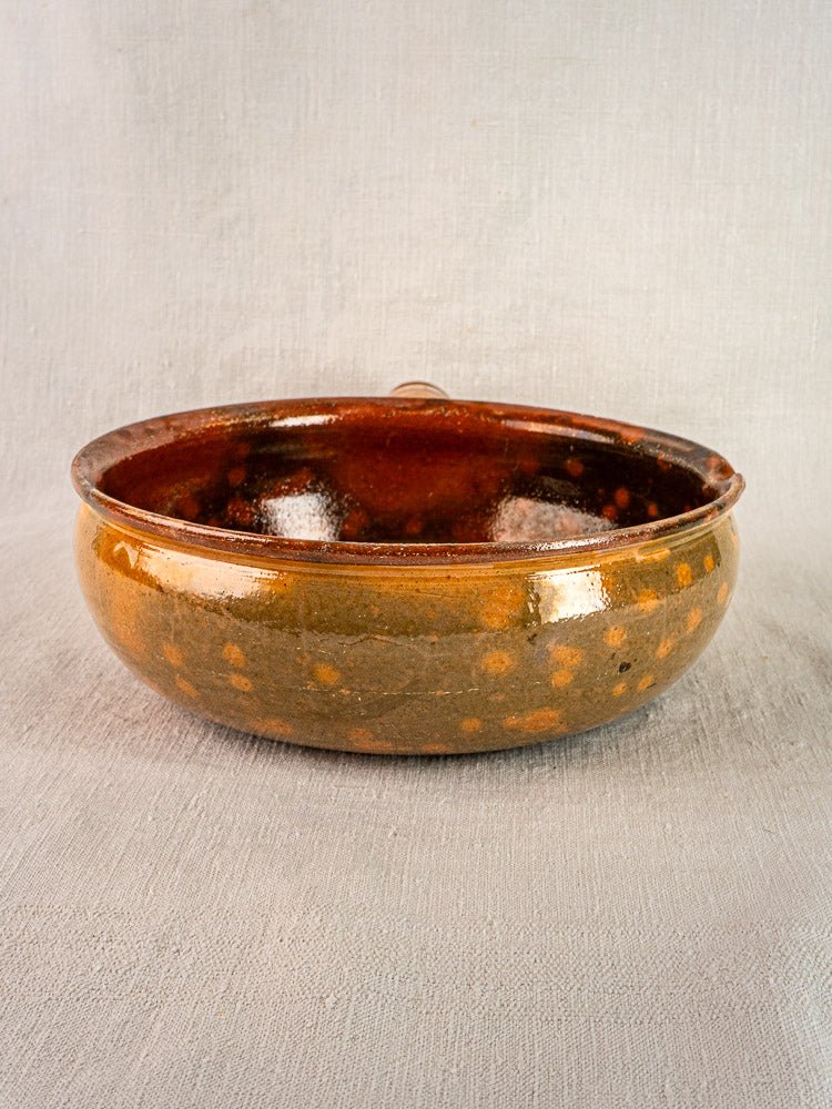 Antique French terracotta Vallauris poêlon with glossy brown jaspé glaze on light gray surface.
