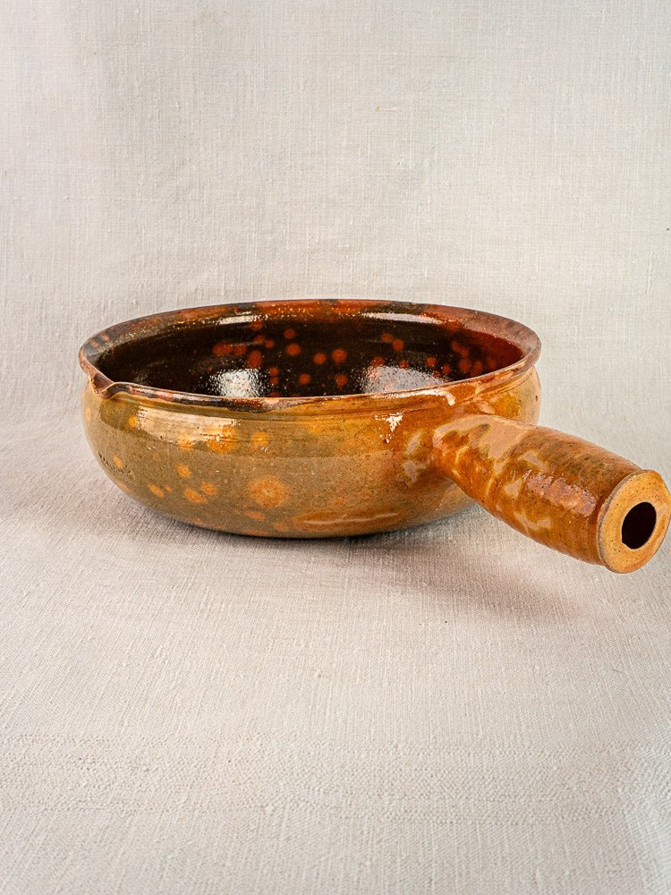 Antique Vallauris Jaspé French terracotta poêlon with brown glaze, side handle, and spout on fabric.