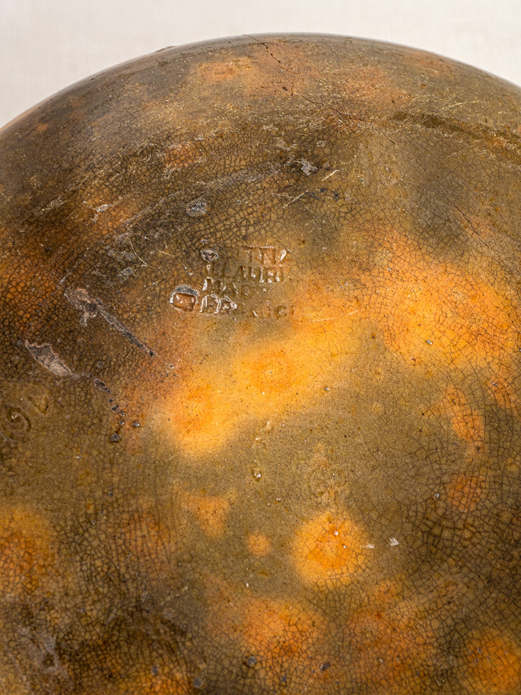 Weathered circular Vallauris ceramic with orange-brown crackled glaze and faint central maker’s stamp.