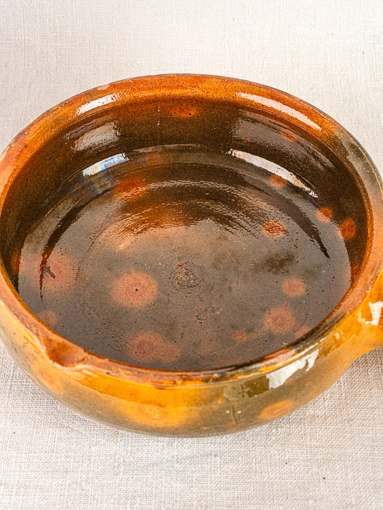 Antique French Vallauris terracotta poêlon, circa 1900–1930s, brown glazed ceramic on textured fabric.