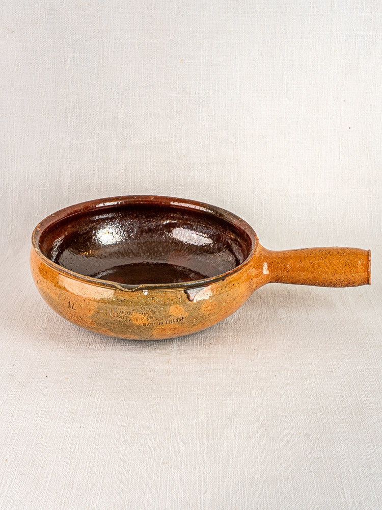 Antique French Vallauris poêlon with brown ceramic finish and long handle, side view.
