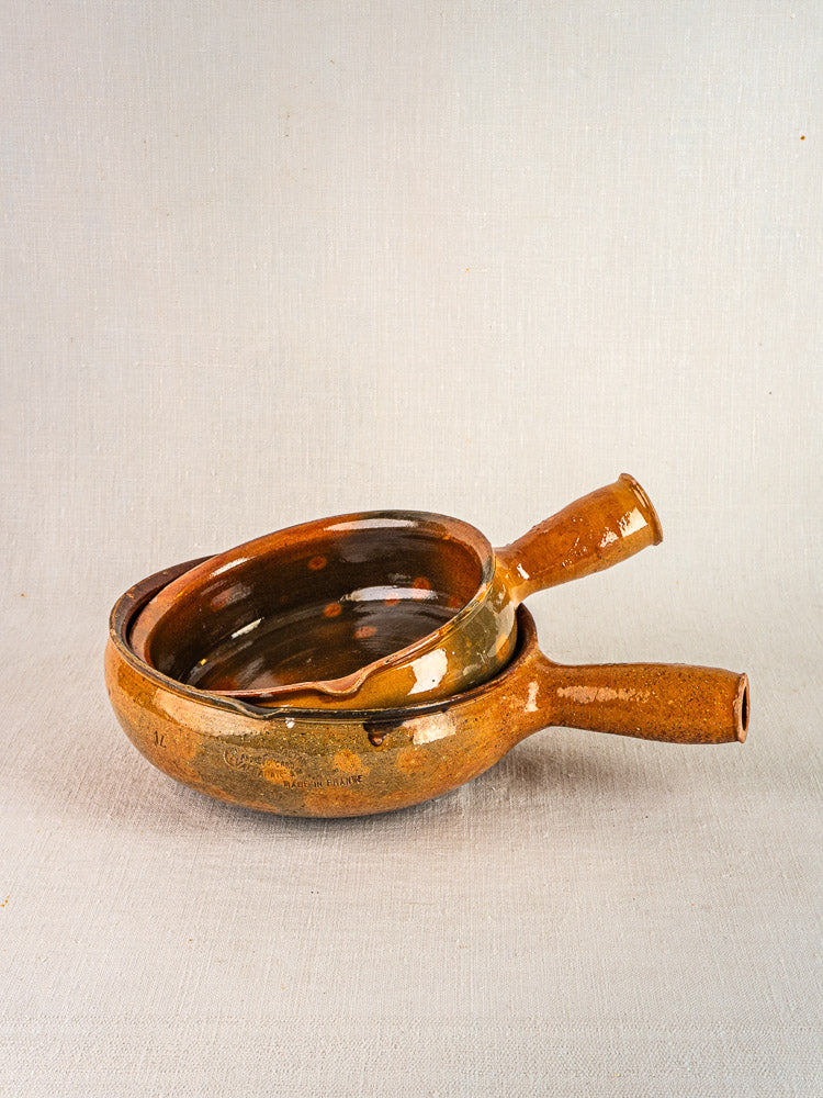 Antique French Vallauris terracotta poêlons with brown ceramic handles, nested on light gray textured surface.