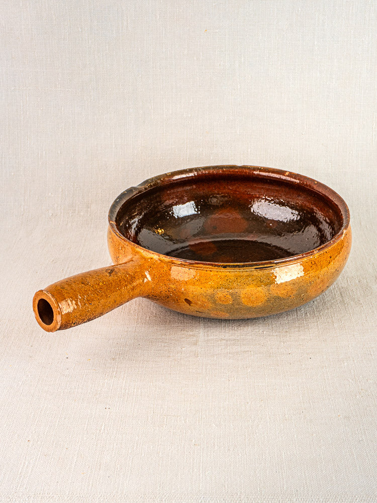Antique French Vallauris terracotta poêlon with brown-glazed round body and spout handle on neutral surface.