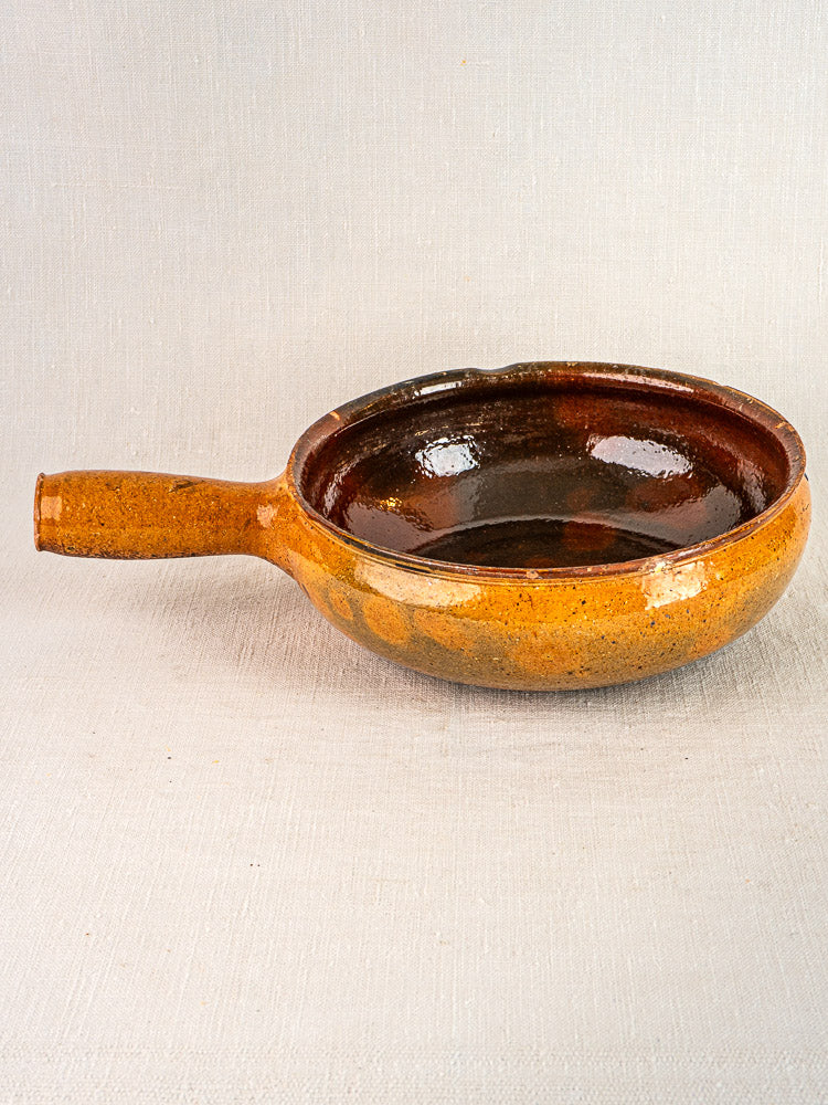 Pair of antique French Vallauris terracotta poêlons with glossy interiors on light fabric background.