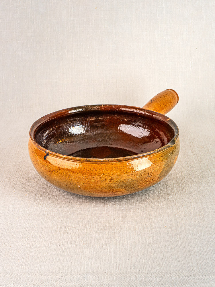 Pair of antique French Vallauris terracotta poêlons with brown glaze and short handles on light surface.