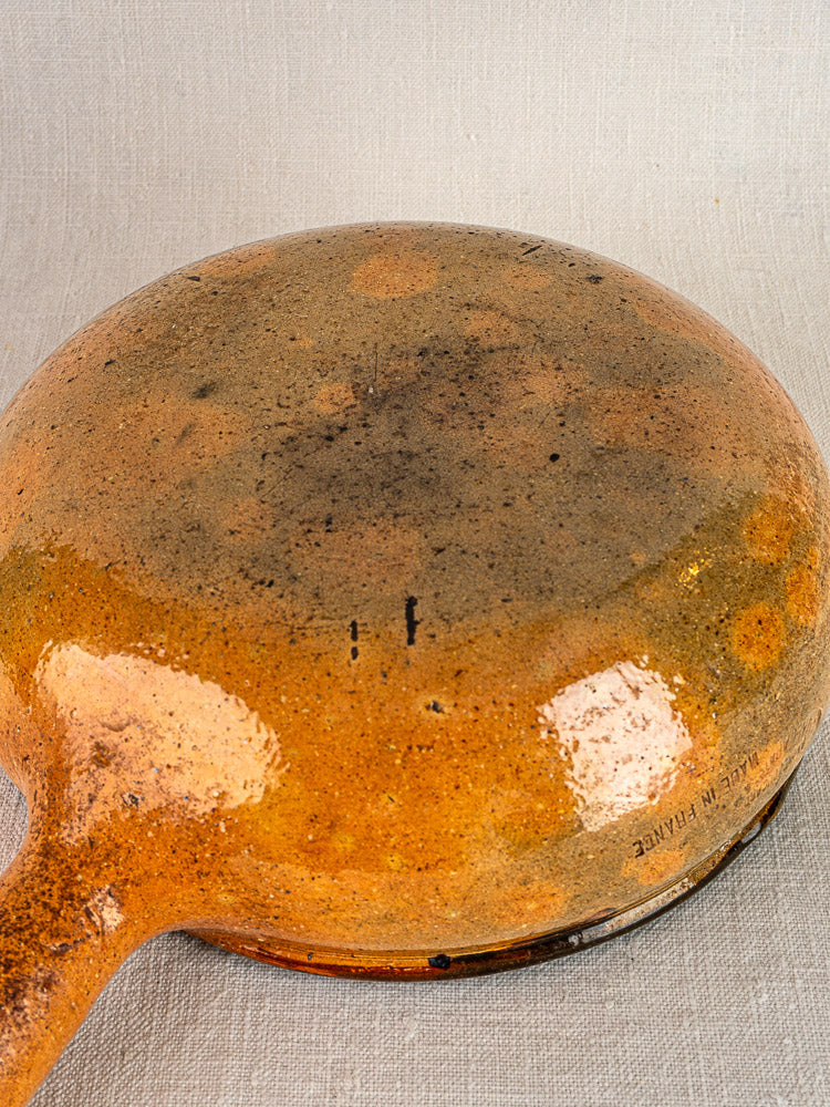Bottom of antique French Vallauris terracotta poêlon pair, worn and stained, on textured fabric.
