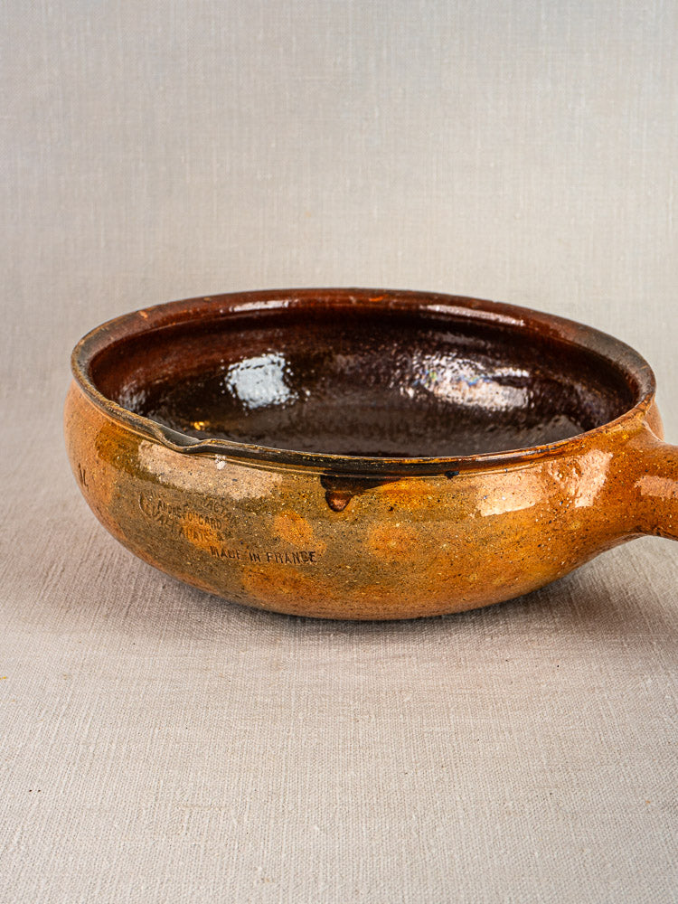 Antique French Vallauris terracotta poêlon with brown glaze and handle on neutral surface.