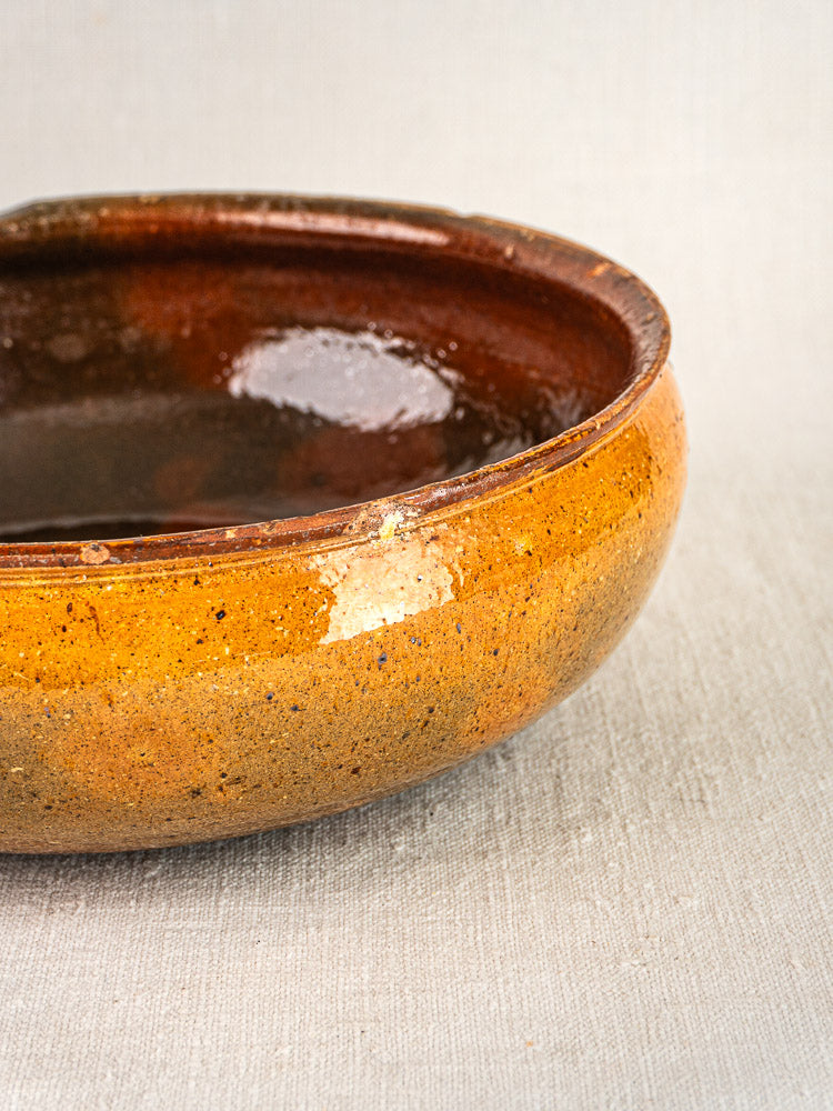 Antique French Vallauris terracotta ceramic bowl with glossy brown interior and matte orange exterior on textured surface.