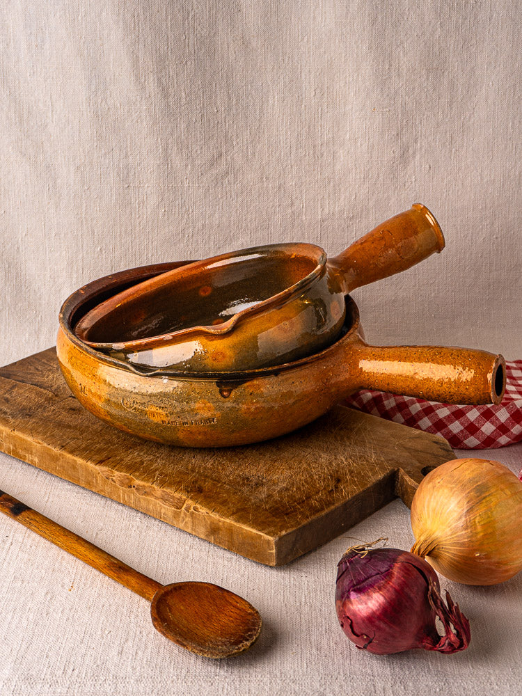 Pair of antique French Vallauris terracotta poêlons stacked on a wooden board with kitchen accents.