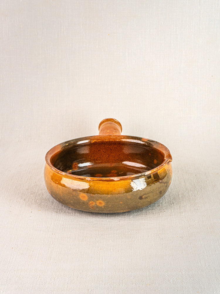 Antique French Vallauris poêlon, round terracotta ceramic with spout and handle on neutral fabric.