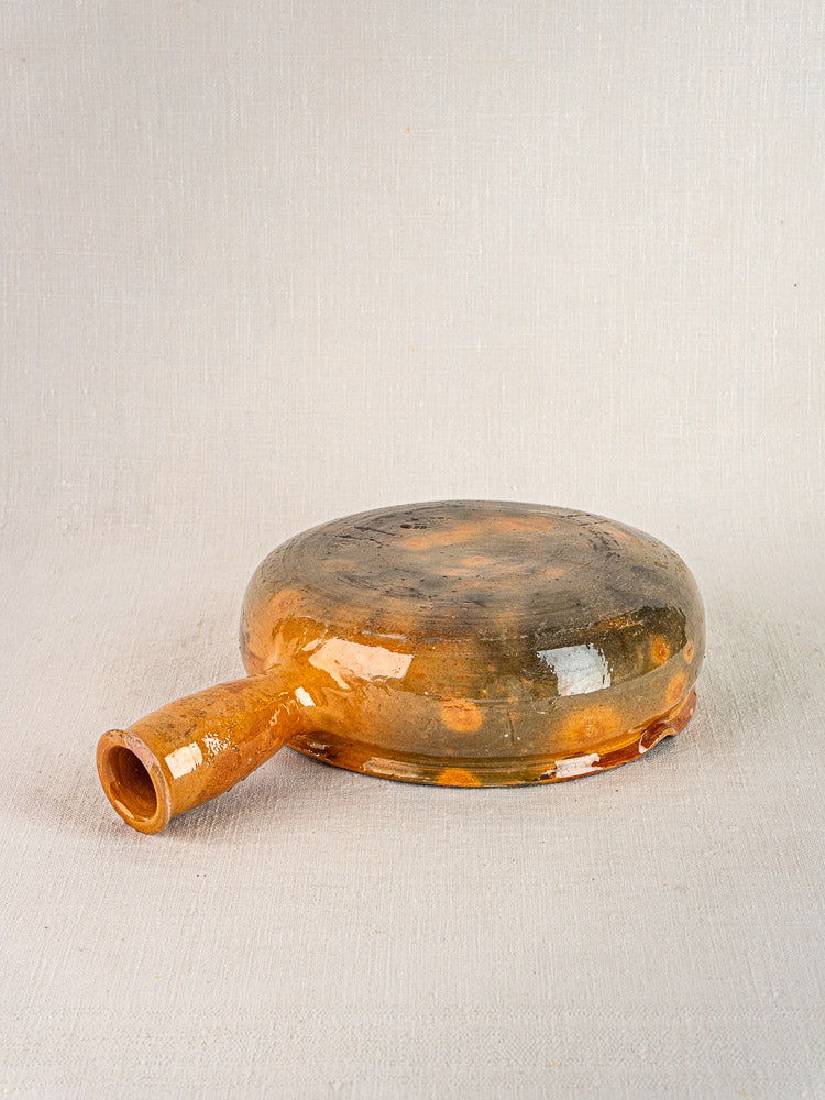 Antique French Vallauris poêlon, circa 1900–1930s, brown glazed terracotta on light fabric.