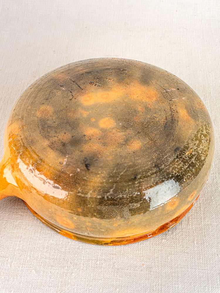 Underside of antique French Vallauris terracotta poêlon with patina on light fabric background.
