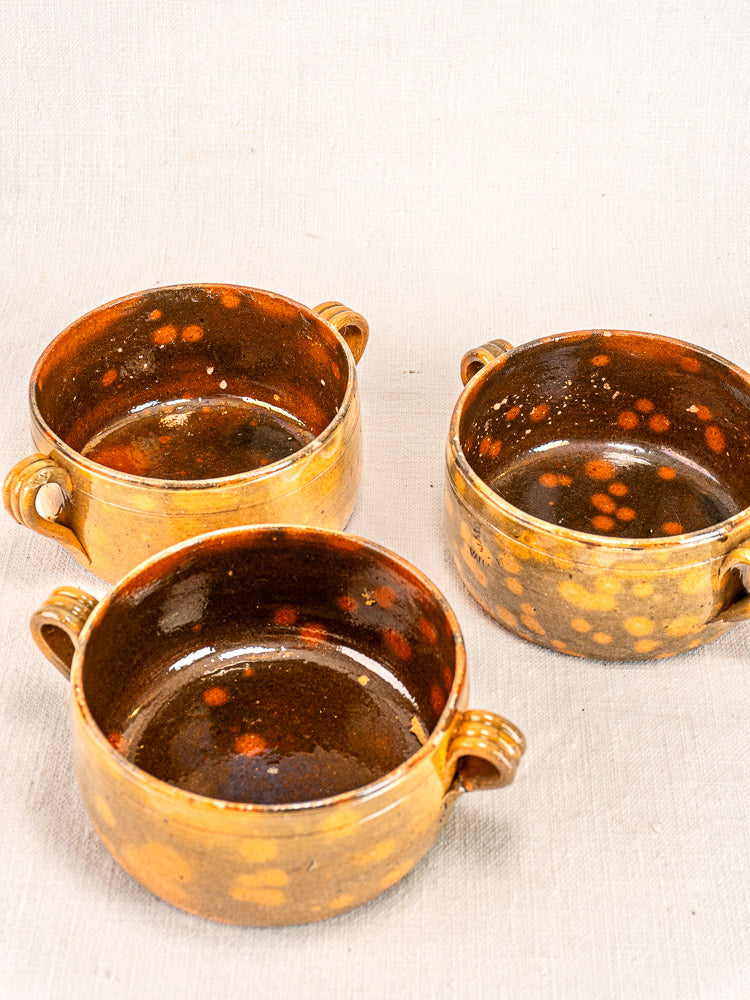Set of three French Vallauris earthenware bowls with brown glaze, yellow-orange speckles, and handles.