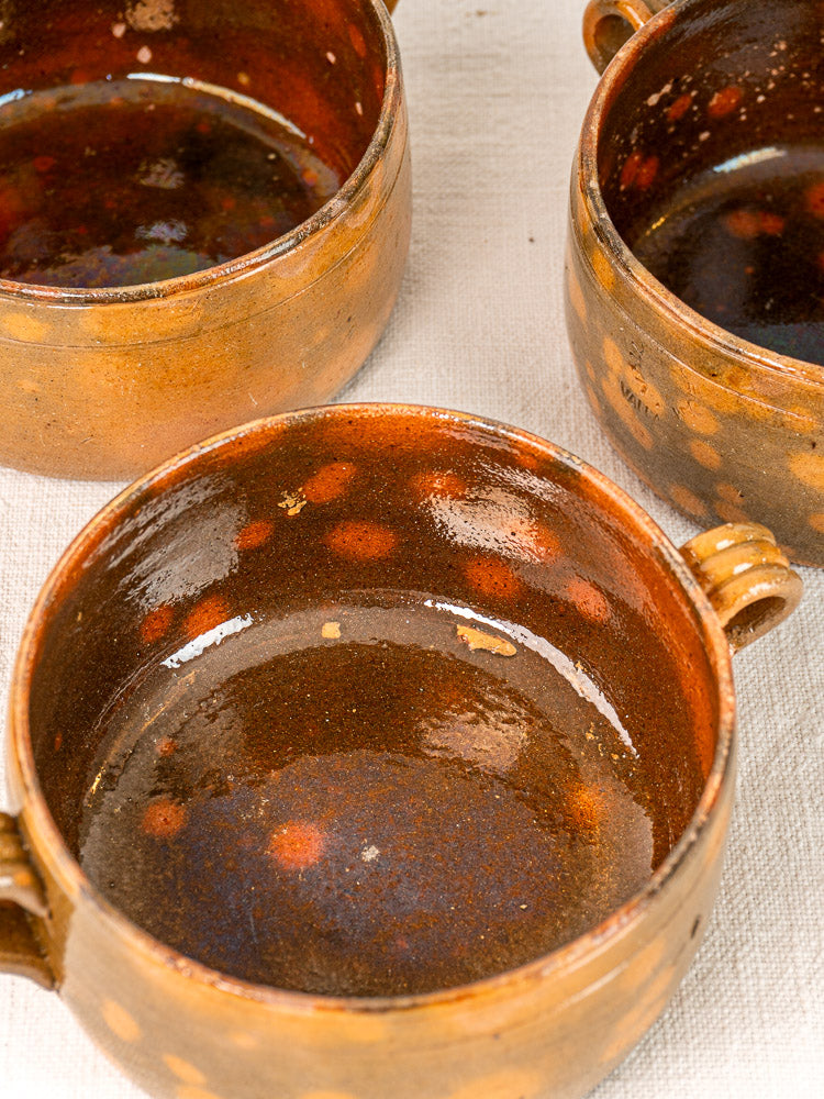 Set of three vintage French Vallauris earthenware bowls with mottled brown and reddish-orange glaze on white textured cloth.