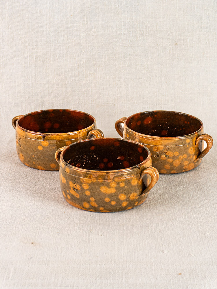 Set of three French Vallauris earthenware bowls with handles in mottled brown and orange on a pale surface.