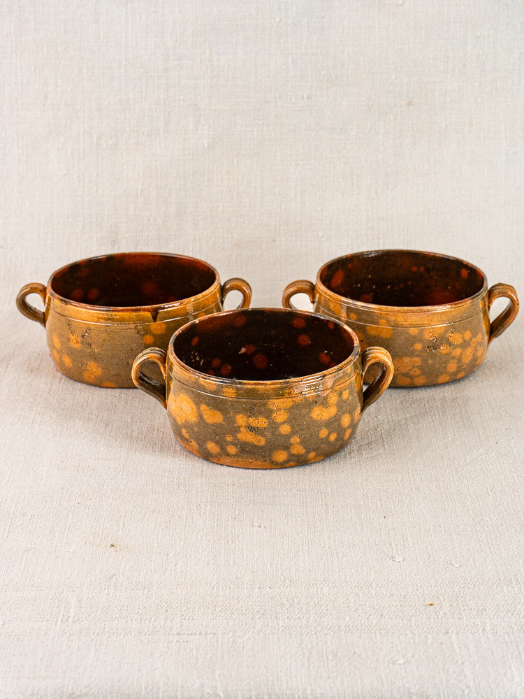 Set of three vintage French Vallauris glazed earthenware bowls with twin handles on fabric background.