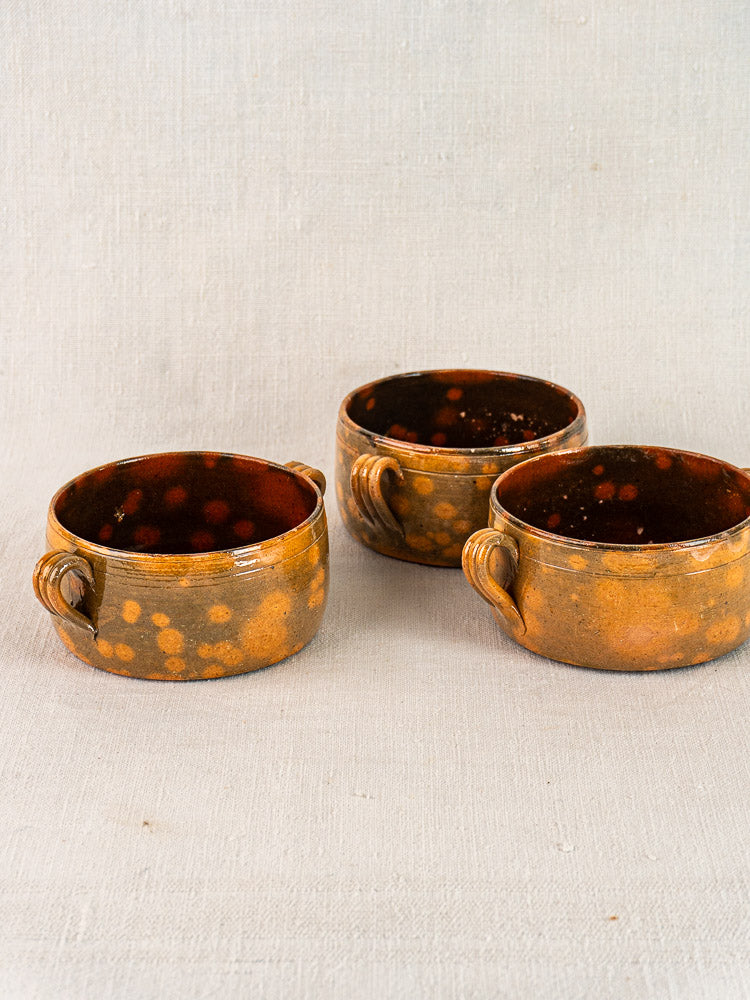 Three vintage French Vallauris earthenware bowls with mottled brown glaze and orange speckles on textured fabric.
