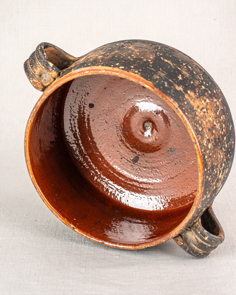 Antique French Vallauris terracotta pot with two handles, weathered exterior, and glossy spiral-glazed interior on light fabric.