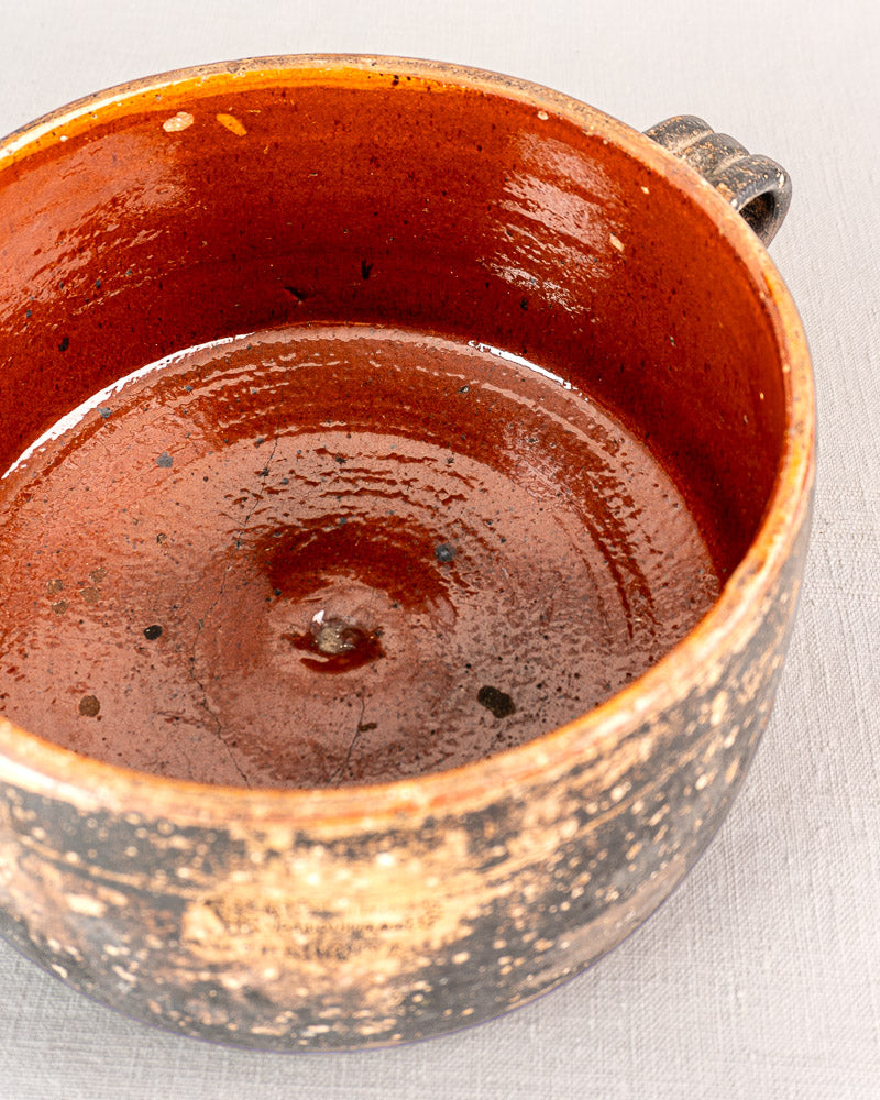 Early 20th-century French Vallauris glazed terracotta pot with round form, black textured exterior, reddish-brown interior, single handle.