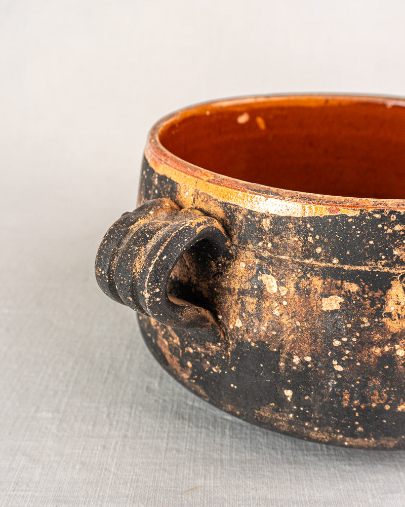 Vintage French Vallauris terracotta cooking pot with single handle, dark brown exterior, glazed reddish-brown interior on light surface.