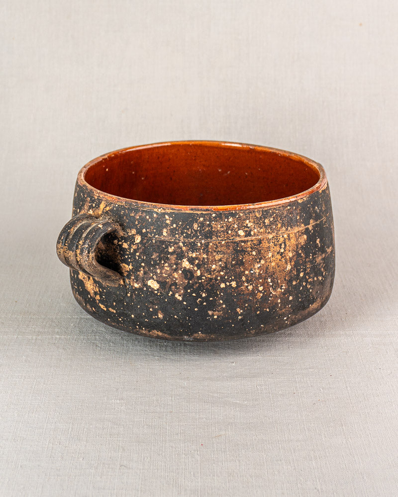 Vintage French Vallauris glazed terracotta pot with round form, dark speckled exterior, and small curved handle on gray textured surface.