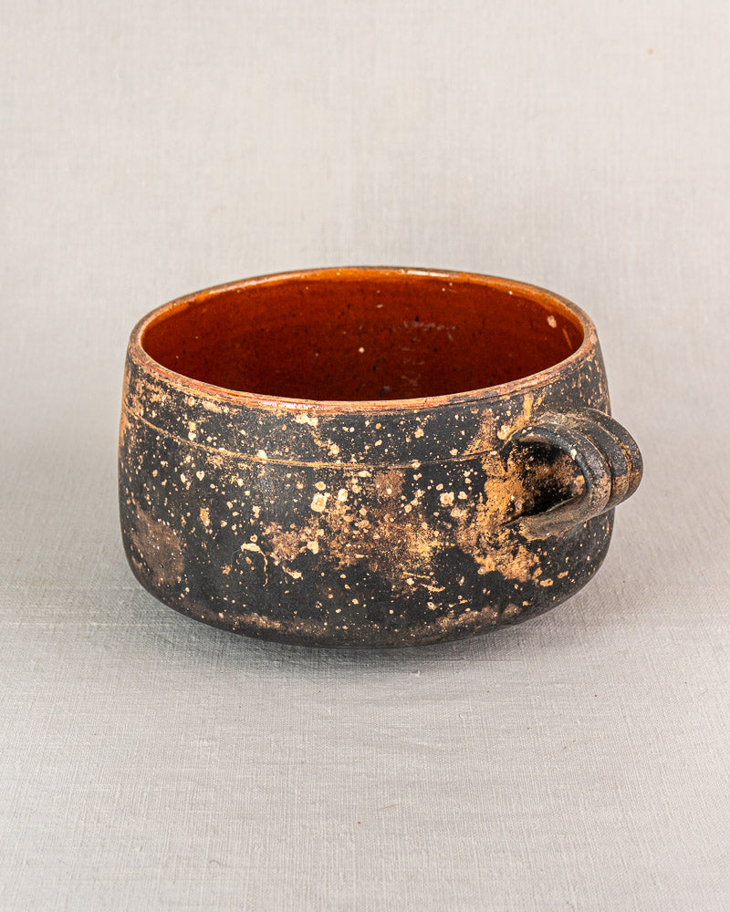 Early 20th-century Vallauris glazed terracotta cooking pot with rustic round shape, single handle, speckled exterior, reddish-brown interior.