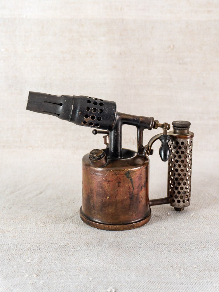 Vintage French blowtorch by Vesta F.J. Paris, circa 1920, with metal tank and perforated handle on light surface.
