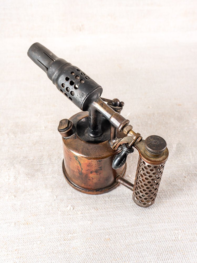 Antique French copper blowtorch by Vesta F.J. Paris with brass fittings and black nozzle on textured surface.