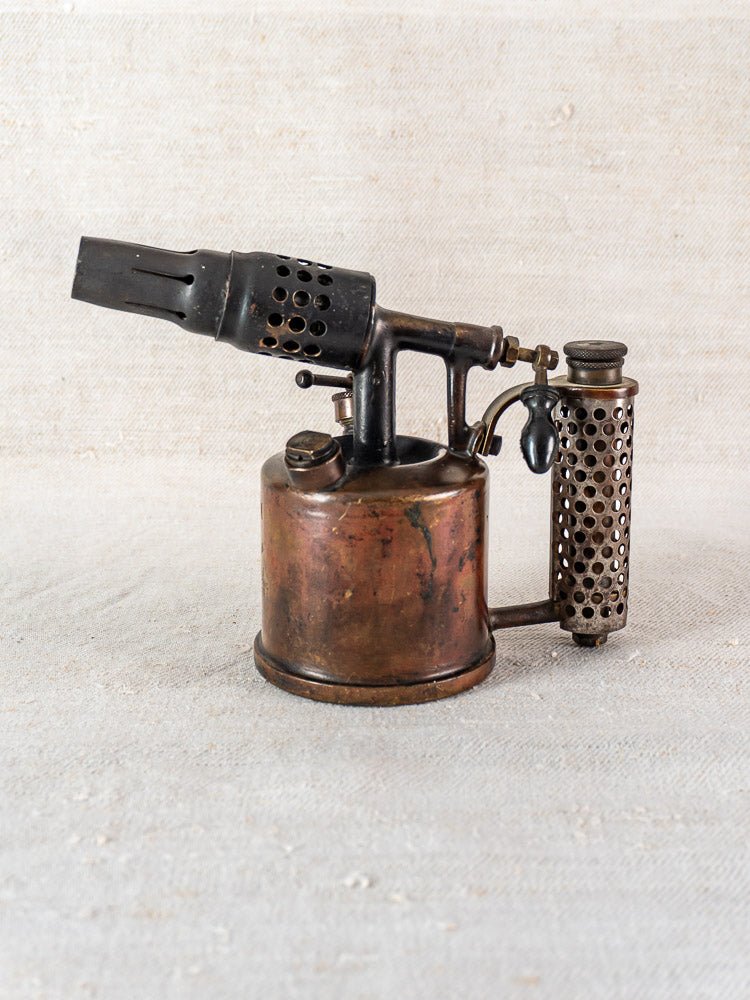 Vintage French Vesta F.J. Paris blowtorch, circa 1920, with cylindrical tank and metal handle on neutral fabric.