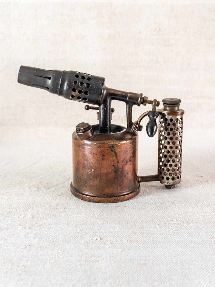 Vintage French blowtorch by Vesta F.J. Paris, brass body and vented handle, on light textured surface.
