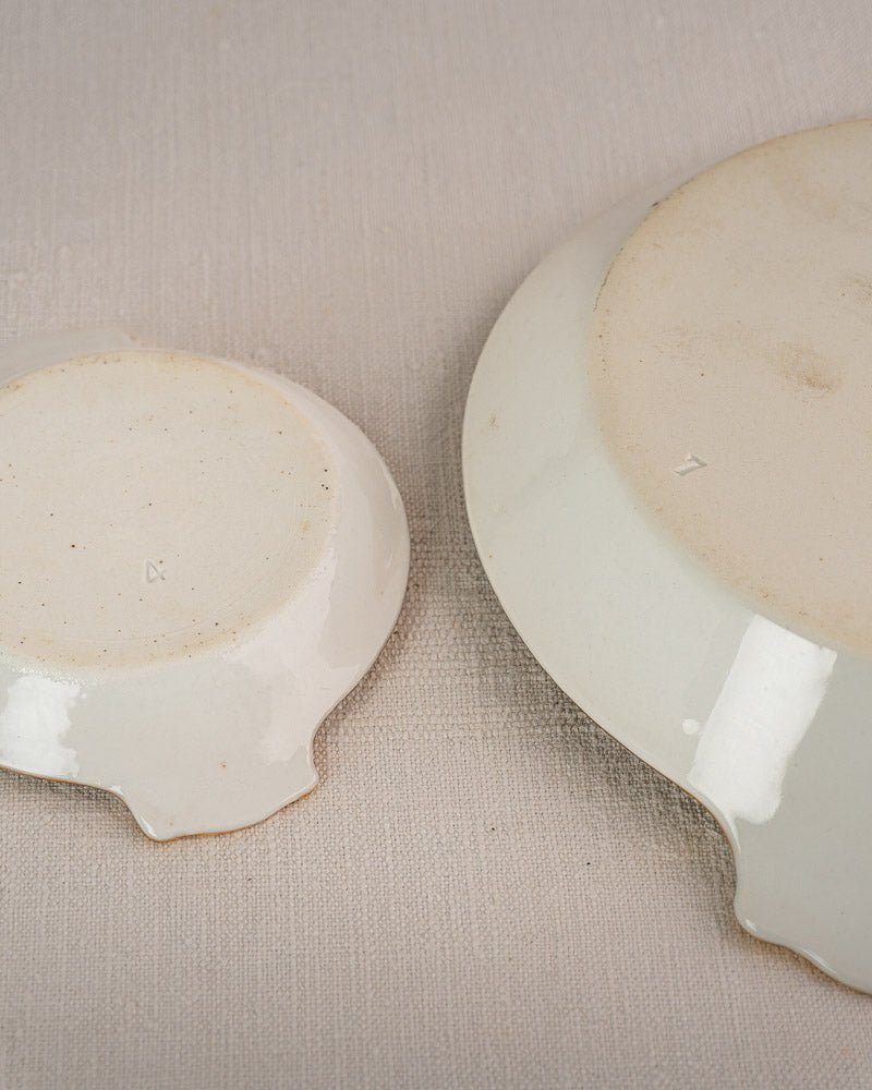 Off-white Vieux Paris porcelain plates upside down, indented edges, on a textured beige surface.