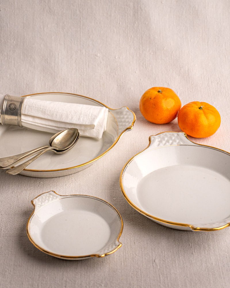 Set of three 19th-century French Vieux Paris porcelain serving dishes with gold rims, on light fabric.