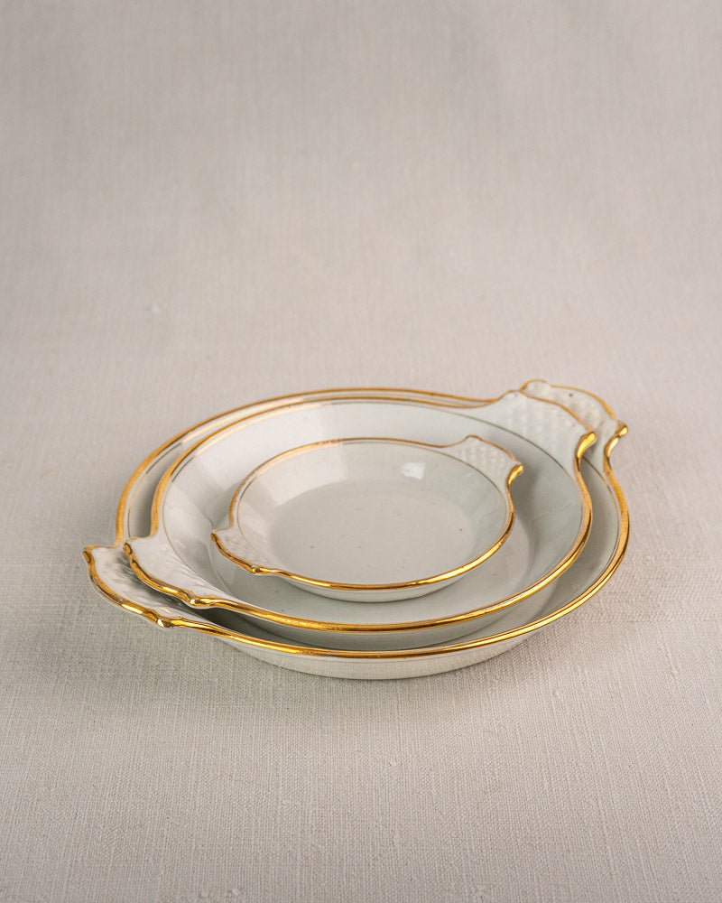 Set of three 19th-century French Vieux Paris porcelain serving dishes with gold trim, on beige fabric.